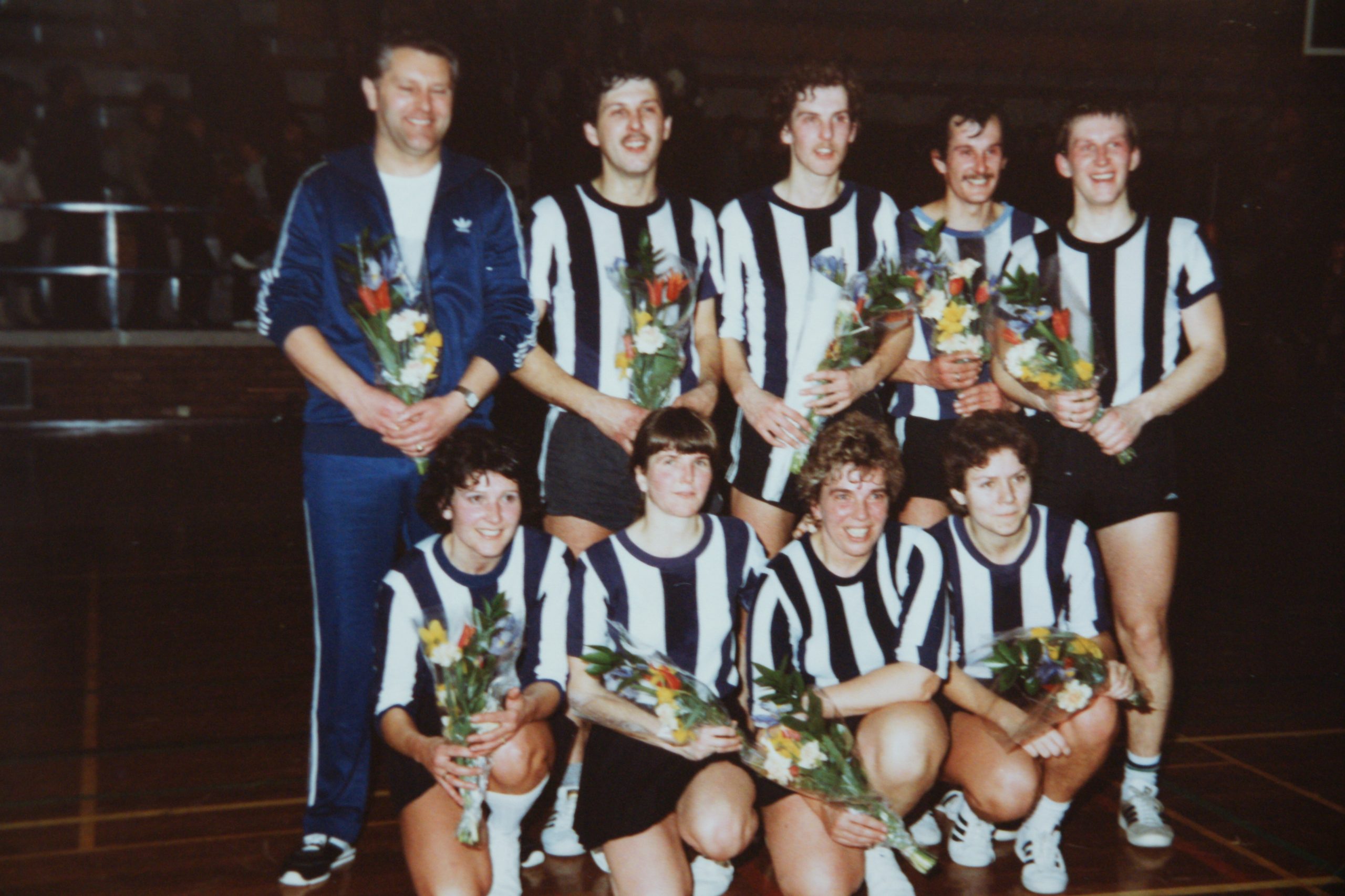 Een Animo-team poseert met bloemen in de sporthal.