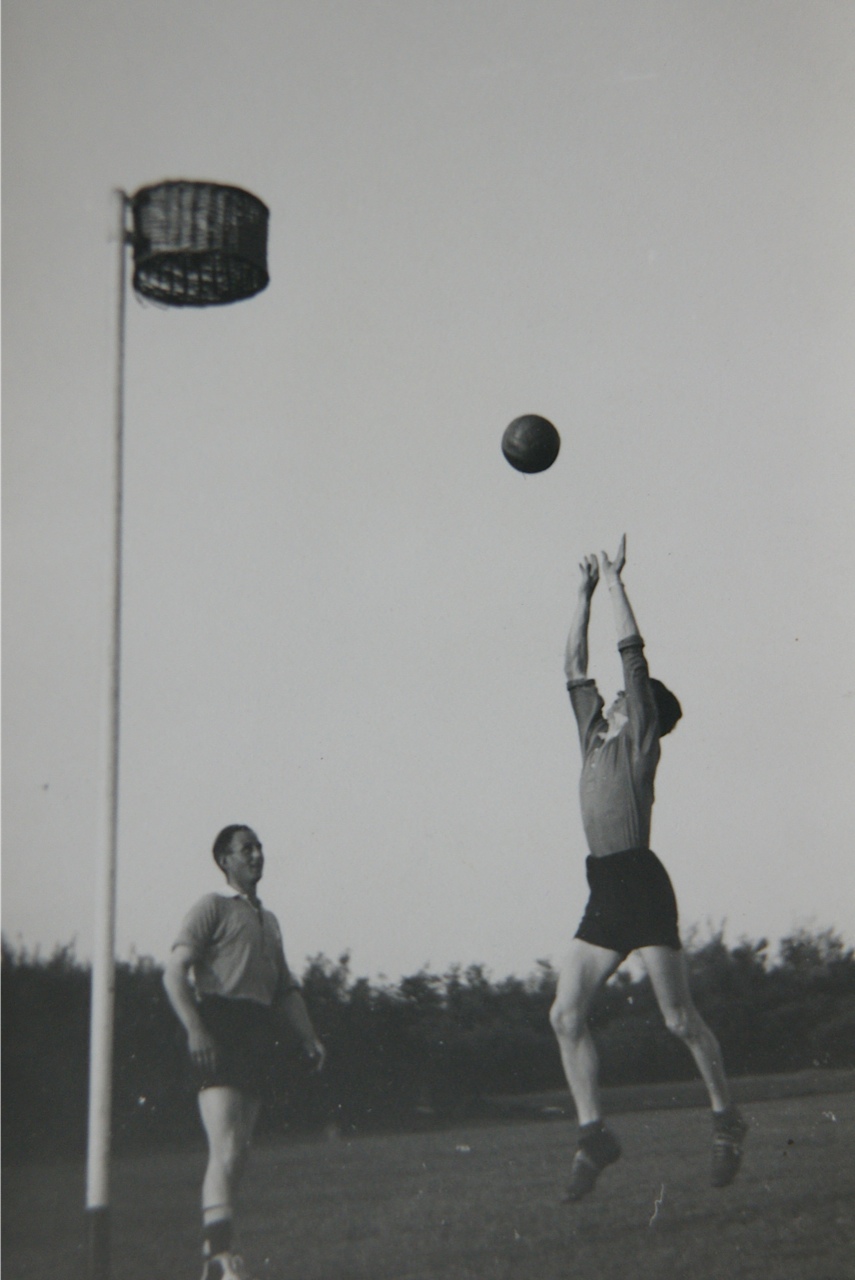 Een speler springt naar de bal bij een korf op het veld.
