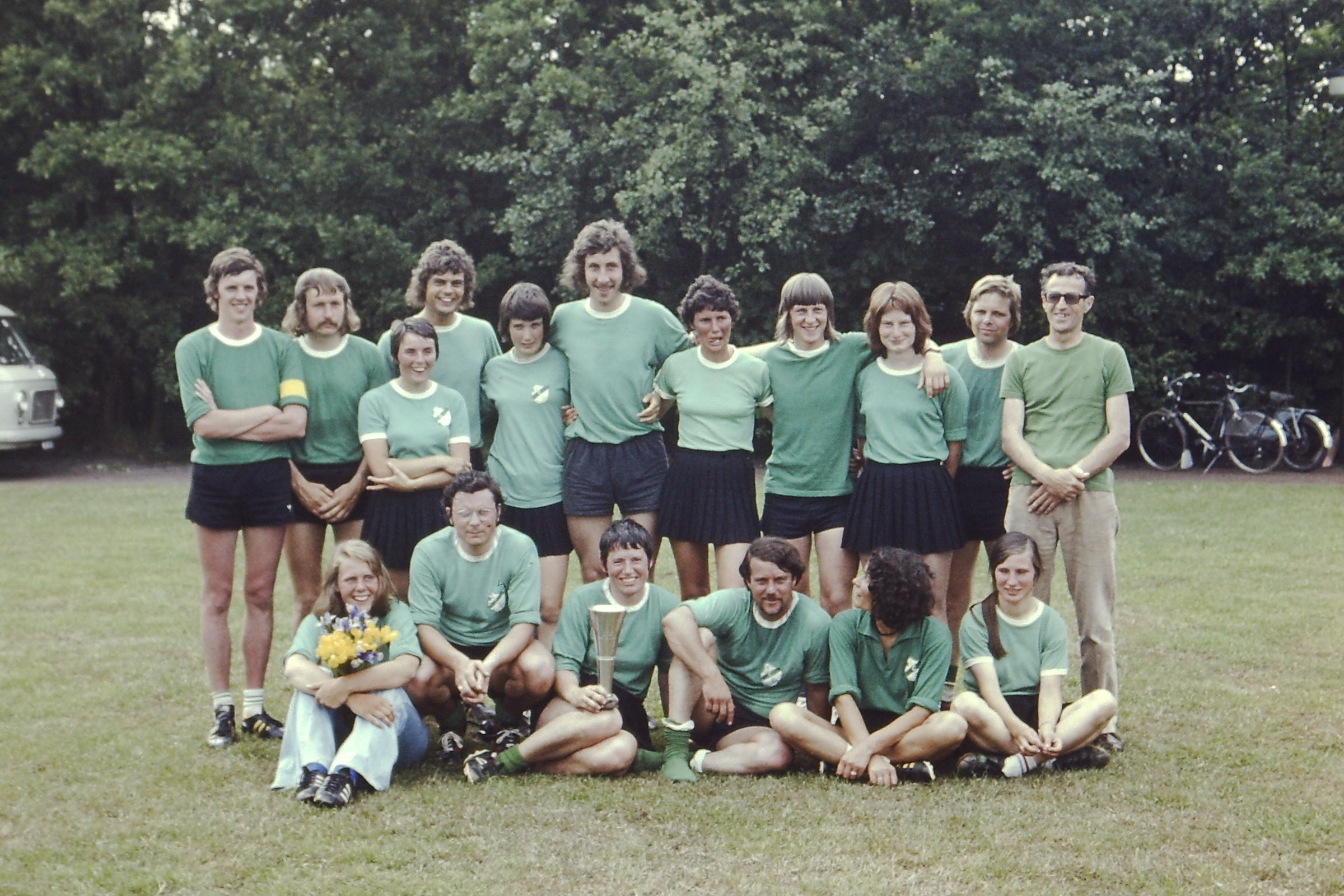 Een gemengd team van Zuidwesters poseert met een beker op het grasveld.